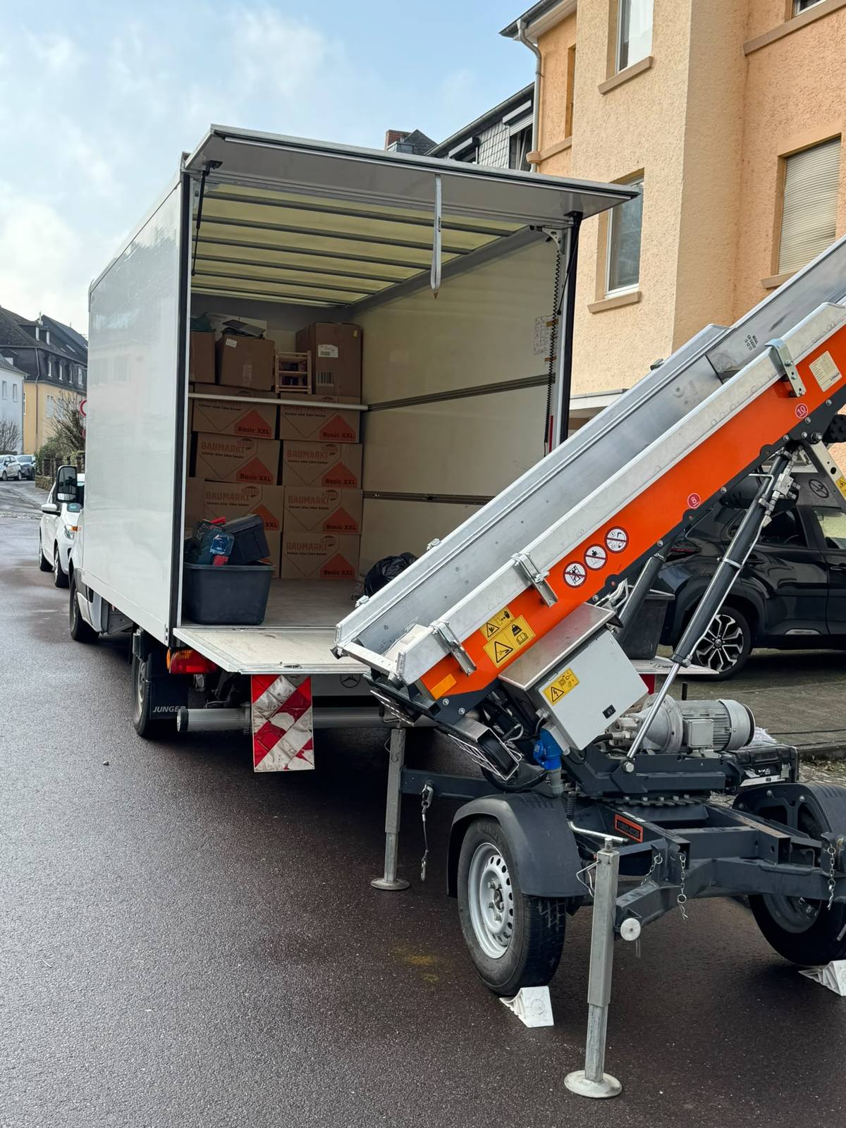 Geöffneter Umzugswagen mit gestapelten Umzugskartons der Größe Basic XXL, davor der Hubarm des Möbellifts vor einem Altbau in Trier