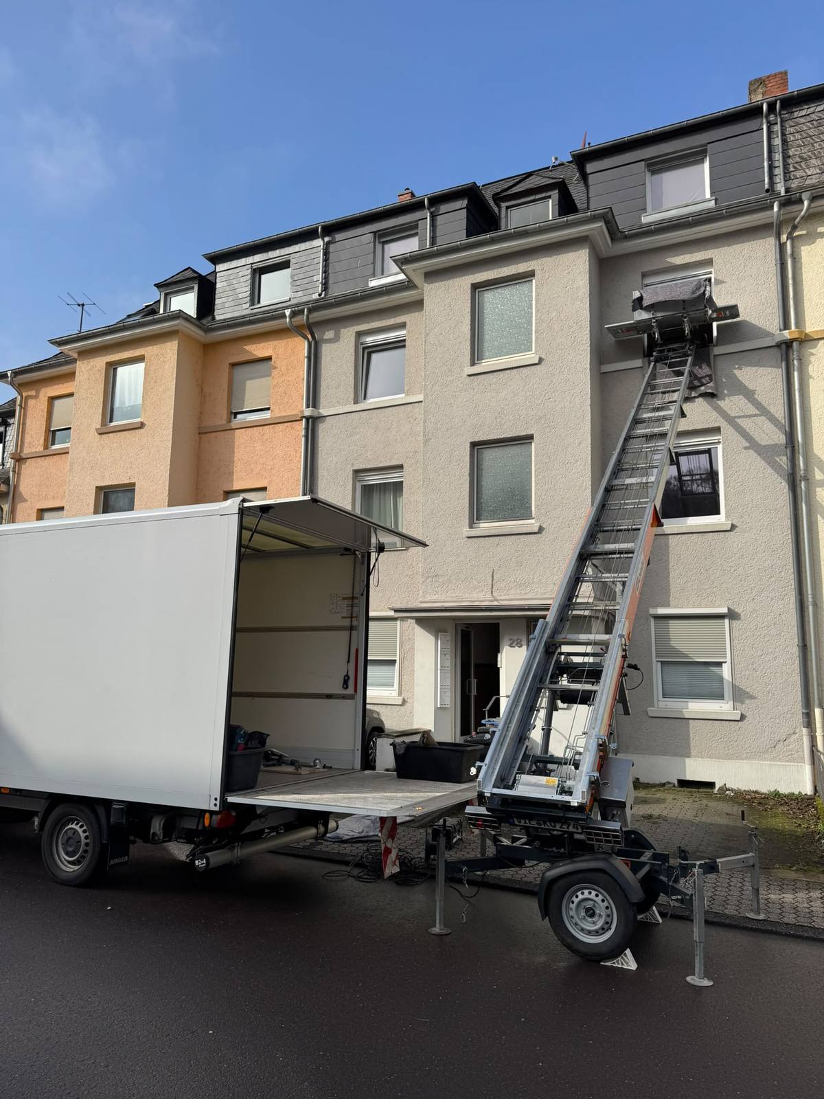 Möbellift von Boels Rental vor einem mehrstöckigen Altbau in Trier, ausgefahren bis zum dritten Obergeschoss, davor ein geöffneter Umzugswagen
